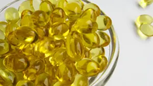 Dzeltenas D vitamīna kapsulas stikla traukā uz gaišas virsmas, simbolizējot uztura bagātinātājus.