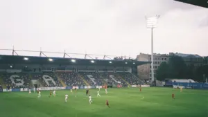 Futbolisti spēlē stadiona laukumā Rīgā, gatavojoties starptautiskajām sacensībām 2026. gada kvalifikācijas ciklā.