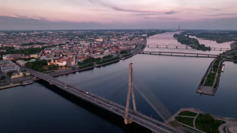 Panorāmas skats uz Rīgas vēsturisko centru un Daugavas upi saulrieta gaismā.
