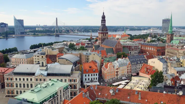 Panorāmas skats uz Rīgas vecpilsētu ar Daugavas upi un tiltiem fonā.